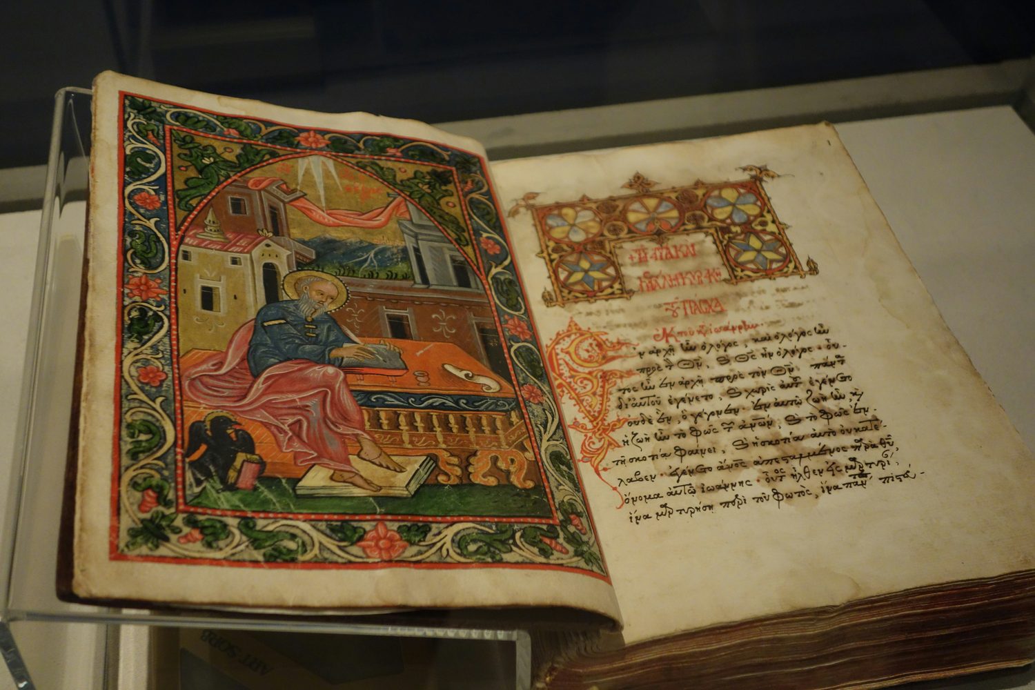 An illuminated Byzantine Gospel manuscript open to an evangelist portrait and a page of Greek text.